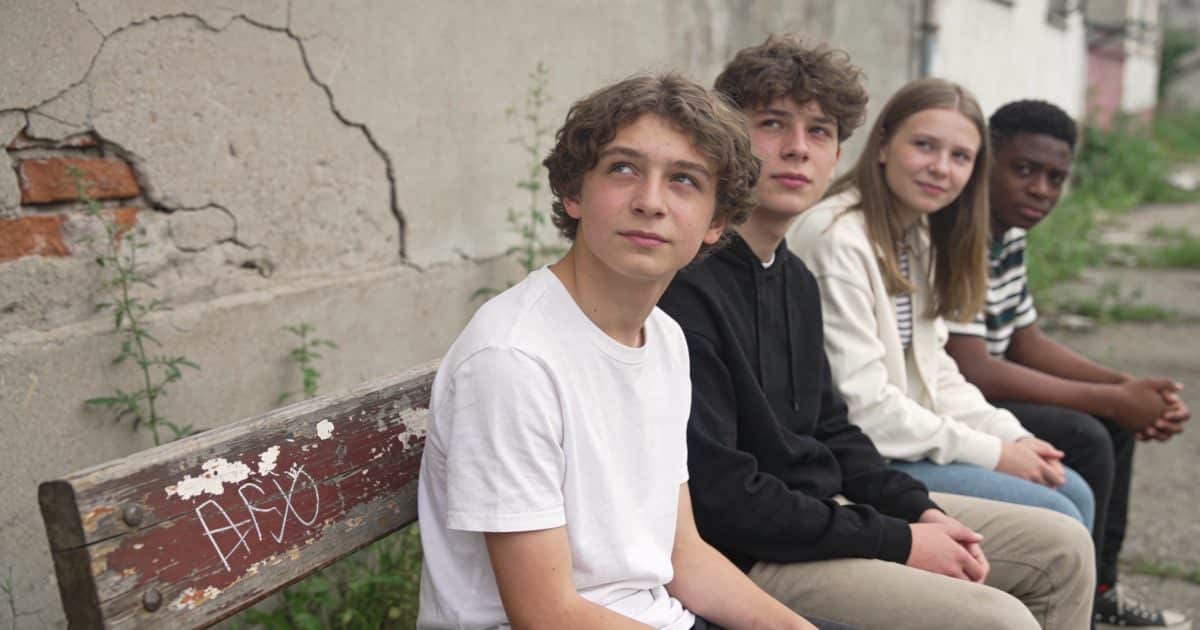 Groupe de jeunes sur un banc en quartier délabré.