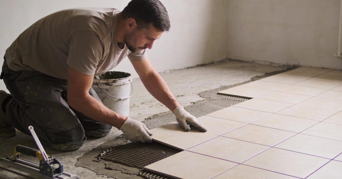Homme agenouille pose des carreaux ceramiques sur sol