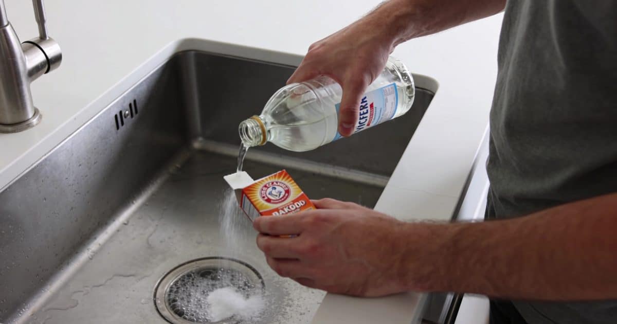 Un homme utilisant du vinaigre et du bicarbonate pour déboucher un évier.