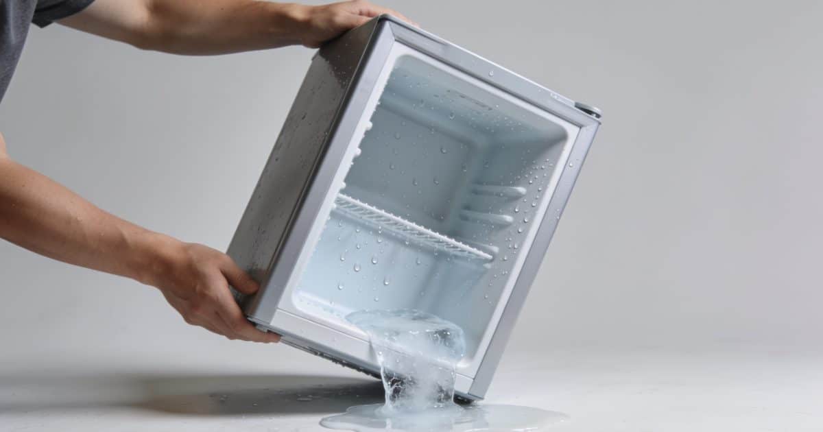 une personne inclinant un congélateur avec de la glace fondue